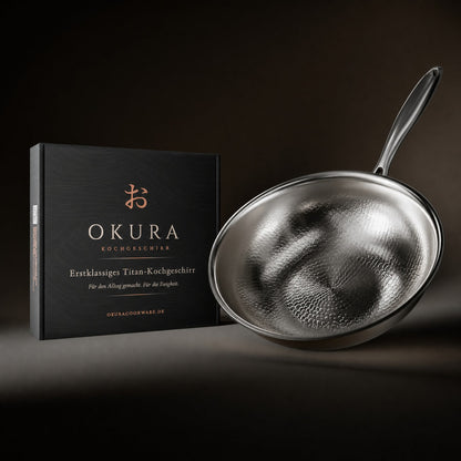Wok pan tilted beside its black gift box with copper lettering, against a dark background. 8