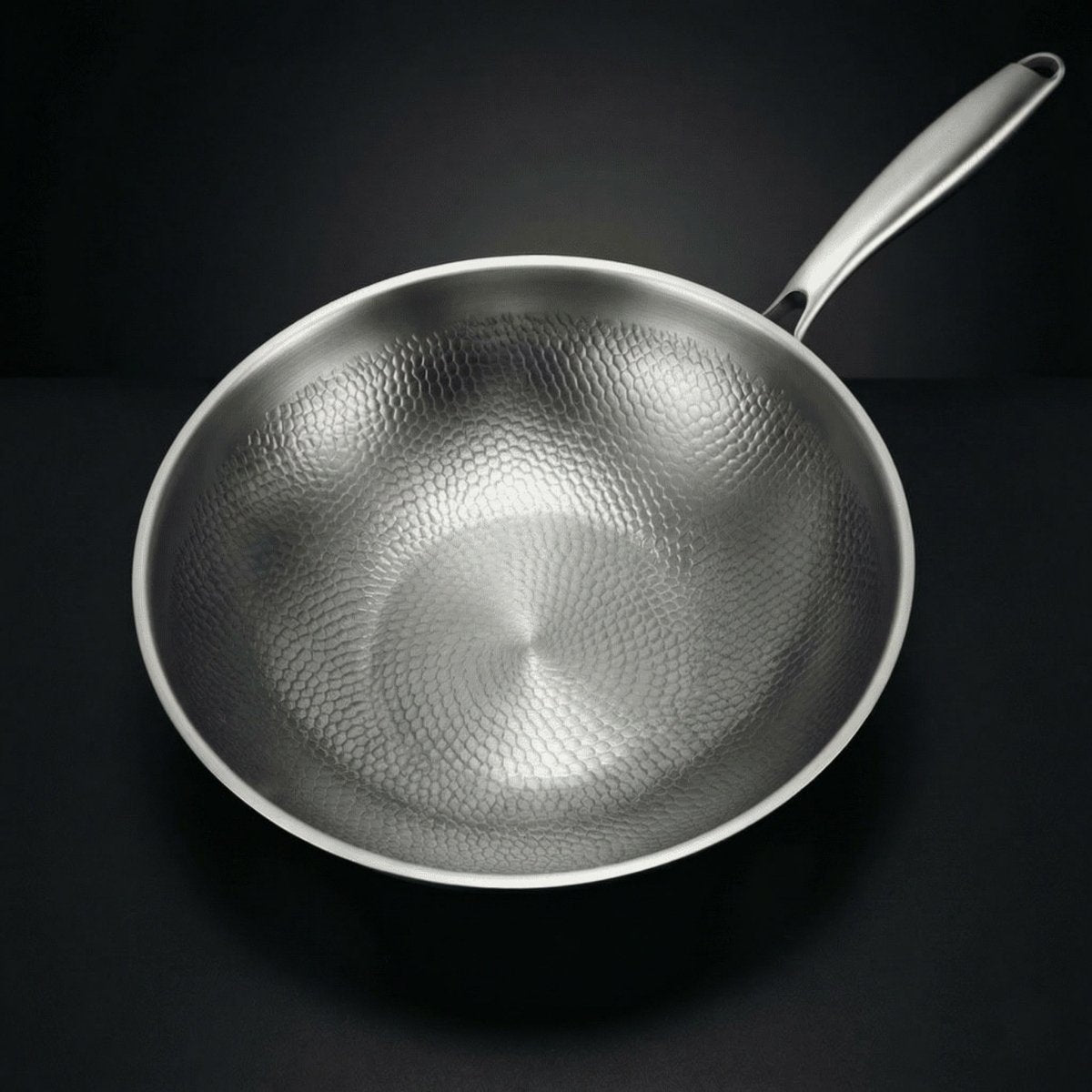Wok viewed from directly above, showing the hammered scale-like pattern across the whole cooking surface and the steel handle. 2