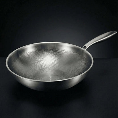 Empty wok seen from a low side angle on a dark surface, showing its hammered interior and long steel handle. 1
