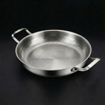 Empty two-handled pan seen from a raised angle on a dark background, showing the textured honeycomb pattern inside and the riveted handles. 1