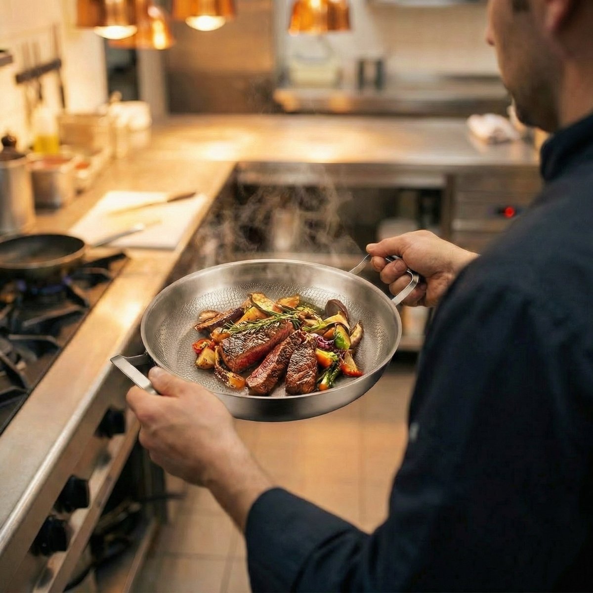 Cook in a professional kitchen holding the pan by both handles, with sliced steak and roasted vegetables steaming inside. 6