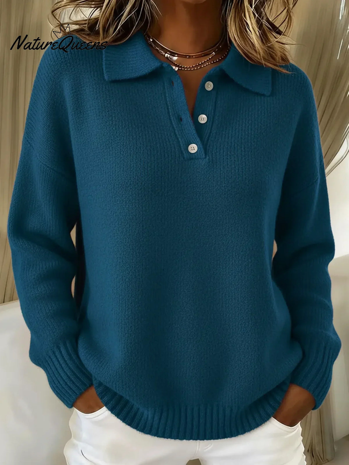 Model wearing the knitted polo jumper in deep teal blue, showing the three-button placket, folded collar and ribbed cuffs. 2