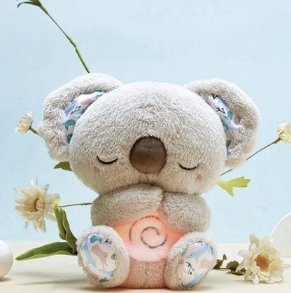 Sleepy grey koala plush with patterned ears and feet and a softly glowing swirl on its tummy, among white flowers. 1