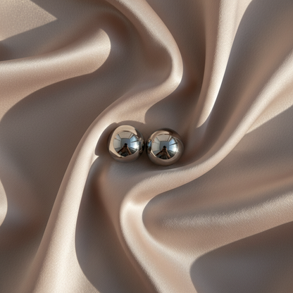 Pair of polished silver magnetic balls resting on softly folded champagne-coloured satin, their shiny surfaces reflecting the room. 1