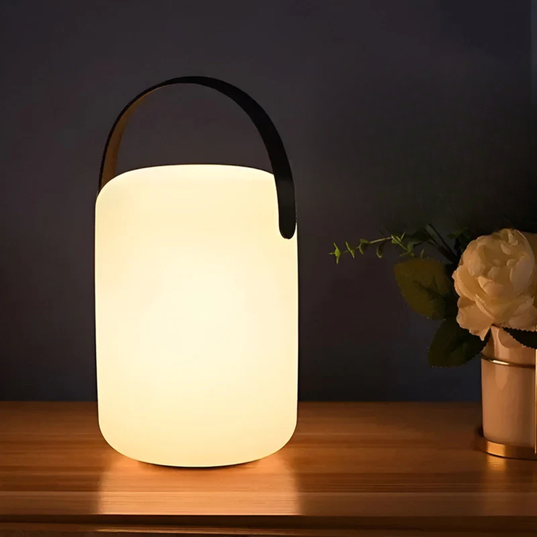 Cylindrical lamp with arched black handle glowing on a wooden shelf beside a white peony 12
