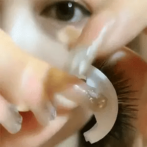 Close-up of a hand holding a curved white lash holder up to an eye, showing the lashes being applied or lifted away. 14