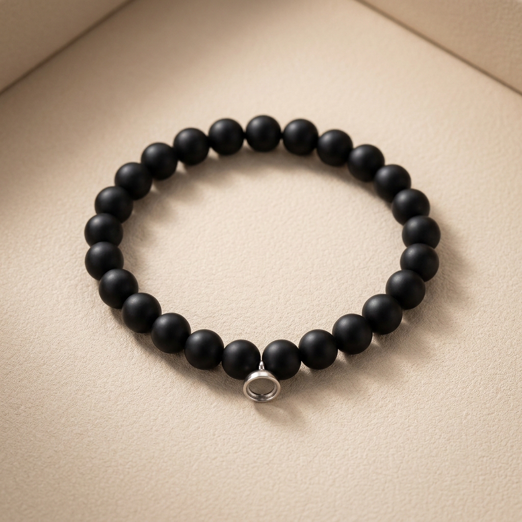 Matte black beaded stretch bracelet with a small silver magnetic clasp, lying on a beige surface 1