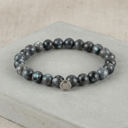 Dark grey bead bracelet with hints of blue-green shimmer and silver clasp on a grey concrete slab 4