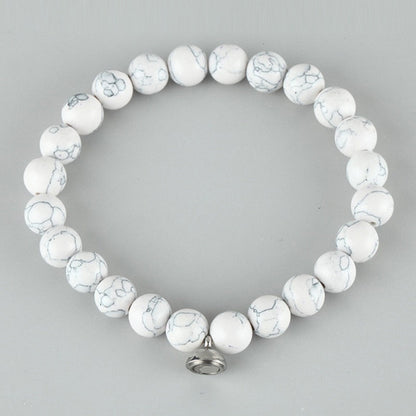 Flat lay of a bracelet of white round beads with grey veining and a small silver charm 3