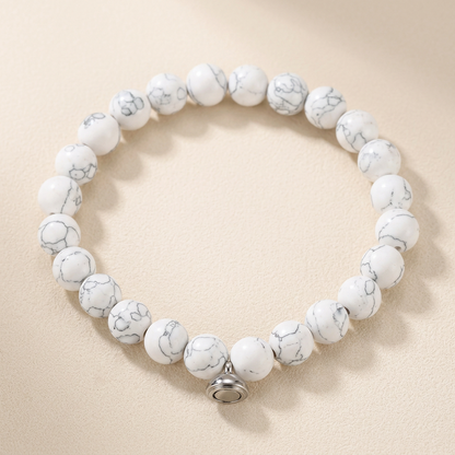 White beaded bracelet with grey marbled veining and a silver magnetic clasp, on a cream background 2