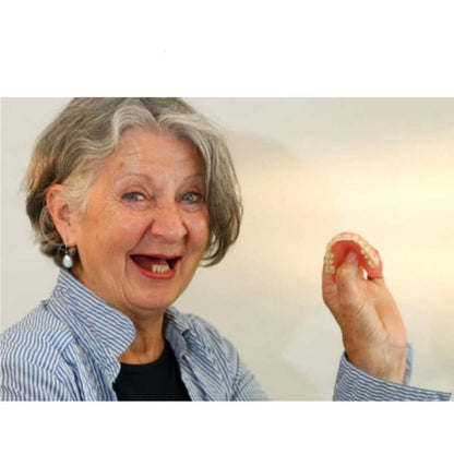 Smiling grey-haired woman in a striped shirt, missing most of her upper teeth, holds up a flexible pink denture. 3