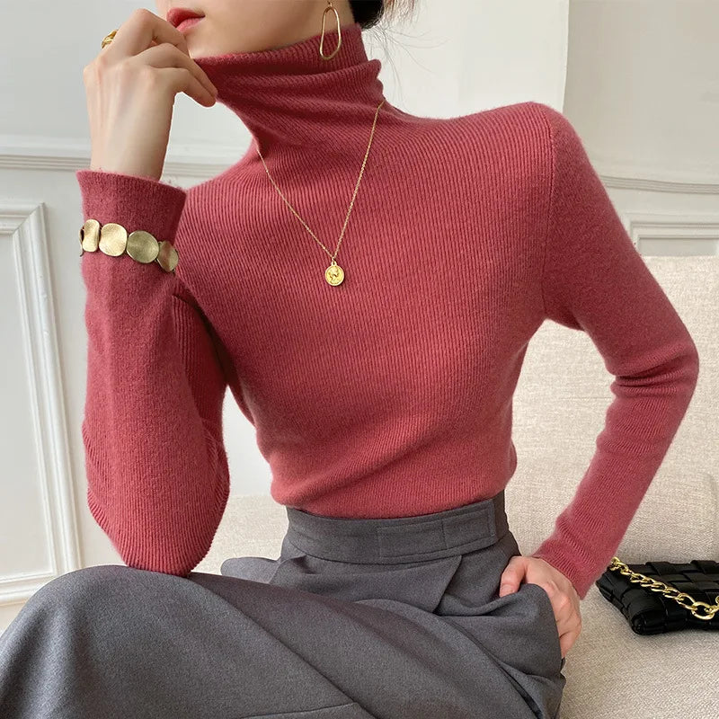 Model wearing the fitted ribbed roll neck jumper in dusky red with a grey skirt and gold bracelet 2