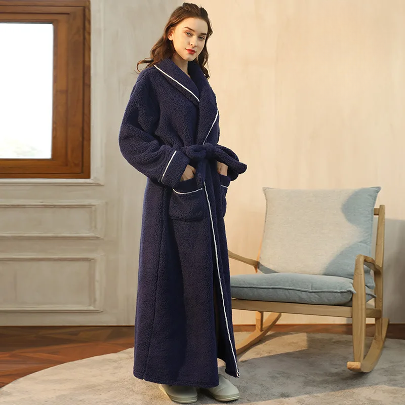 Side view of a navy fleece robe with white piping, hands in pockets, beside a rocking chair 10