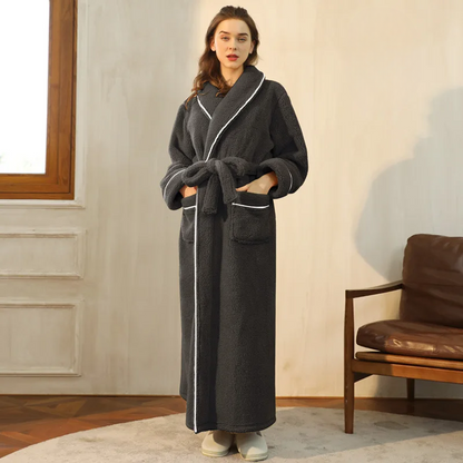 Model in a dark grey fleece robe with white piping, hands in the patch pockets, in a living room 2