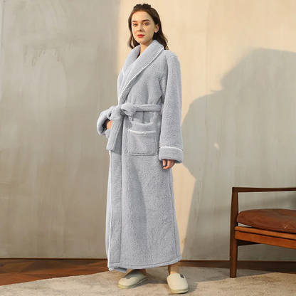Model in a pale grey fleece robe with a knotted belt, standing in three-quarter view by a leather chair 3