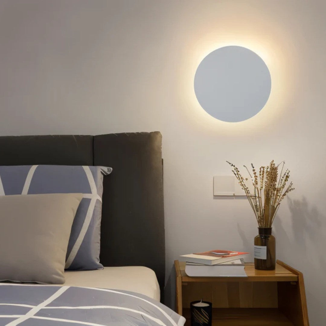 White disc lit on a bedroom wall above a wooden bedside table with dried flowers 7