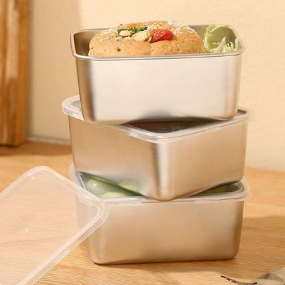 Three steel containers stacked on a wooden surface, the top holding a bread roll with salad, the lower ones sealed with clear lids. 10