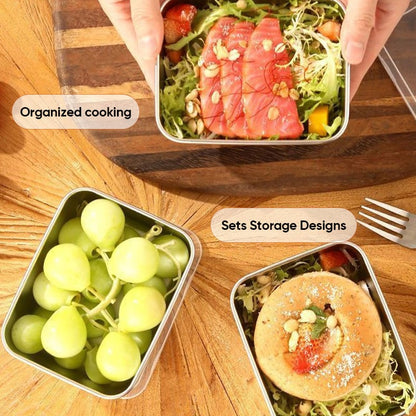 Top-down view of three steel containers on a wooden table holding sliced salmon salad, green grapes and a pastry on salad, with a fork. 8
