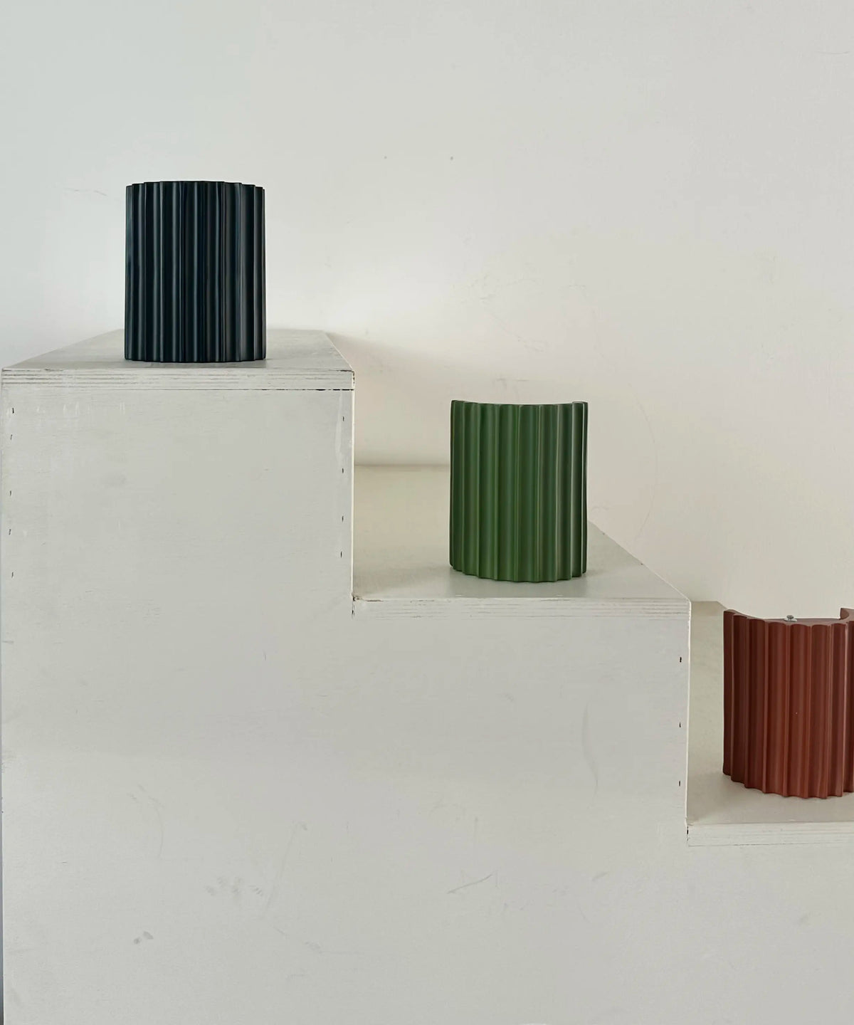 Black, green and terracotta fluted lights displayed on white wooden steps; the terracotta one shows its open back 11