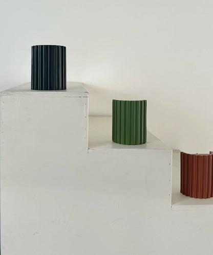 Black, green and terracotta fluted lights displayed on white wooden steps; the terracotta one shows its open back 11