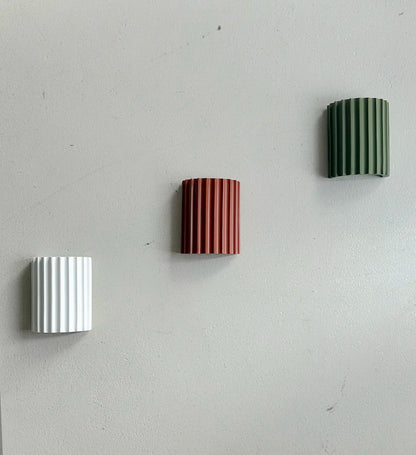 White, terracotta and green fluted wall lights mounted unlit in a diagonal row on a grey wall 12