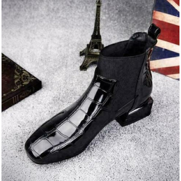 Top-down front view of the glossy black croc-embossed ankle boot with square toe, elastic panel and heel pull tab, styled with small props. 7