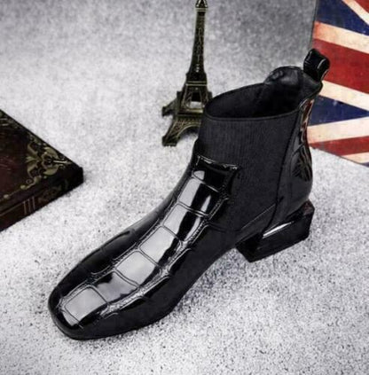 Black croc-effect ankle boot angled from the front, showing the square toe, elastic side panel and low block heel on grey carpet. 5