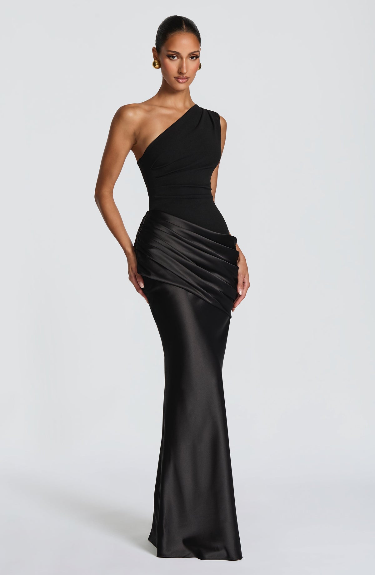 Front view of a black one-shoulder maxi dress on a model, with a pleated crepe bodice and draped satin waist. 22