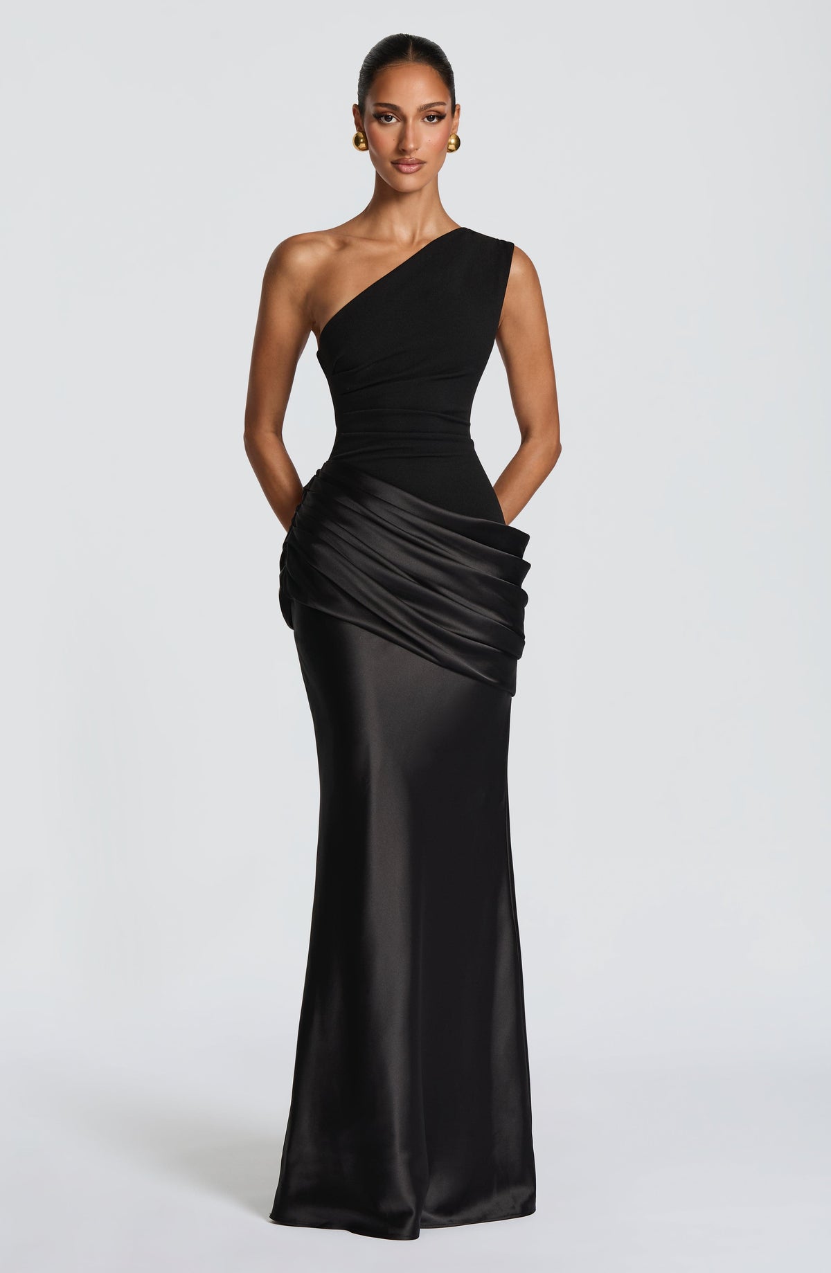 Black version of the one-shoulder dress with gold earrings, showing the matte bodice and glossy draped satin hip and skirt. 20