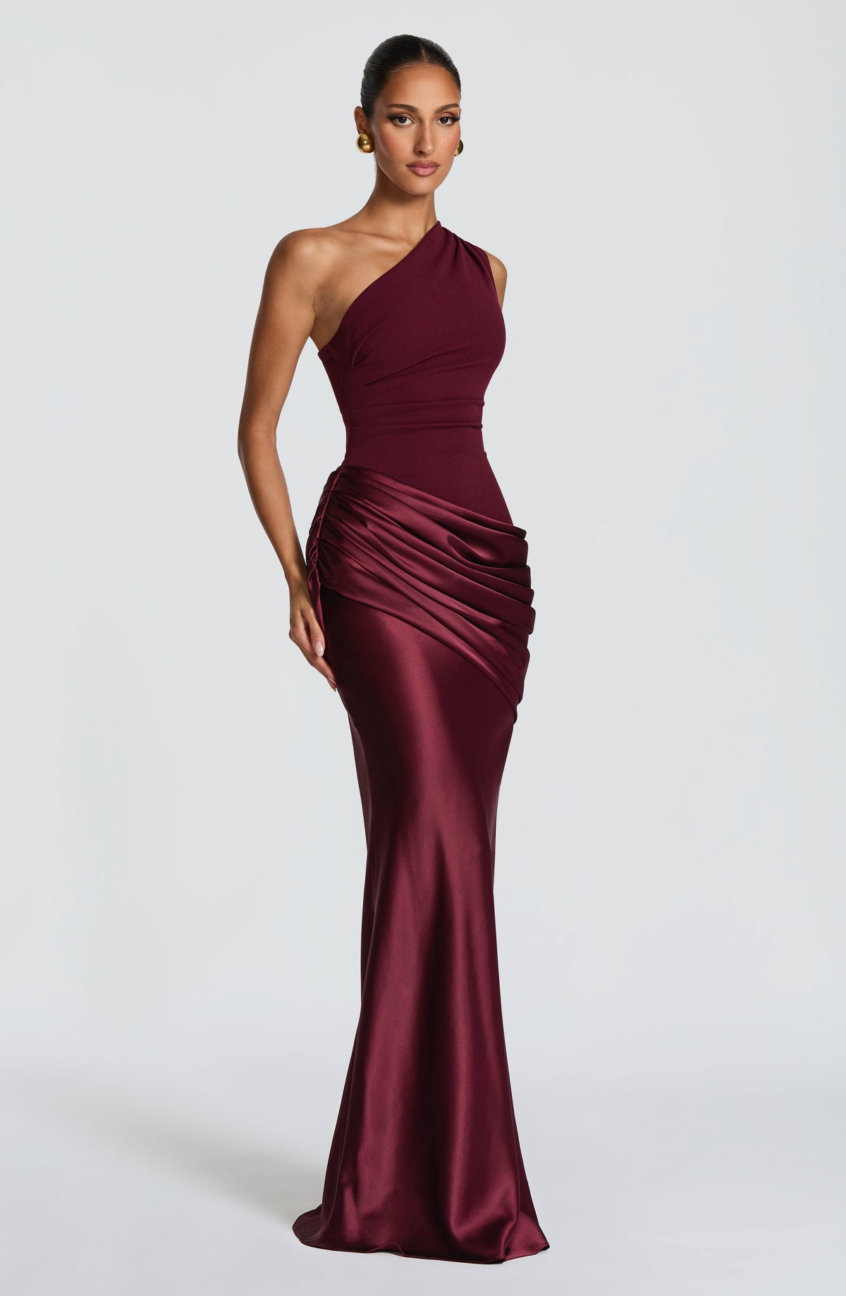 Angled front view of the burgundy one-shoulder dress, showing the gathered detail at the side of the hip and glossy satin skirt. 14