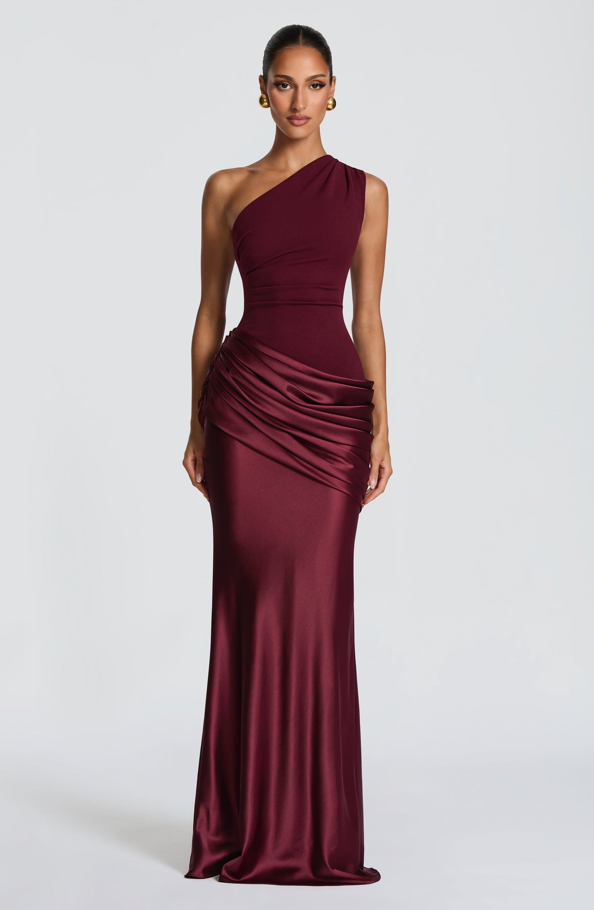 Burgundy version of the dress worn by a model with gold earrings, showing the one-shoulder bodice and draped satin hip. 13