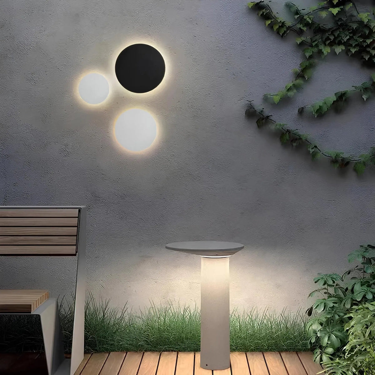 Black and white round disc lights glowing on a textured grey garden wall above a wooden deck, bench and lit bollard. 1