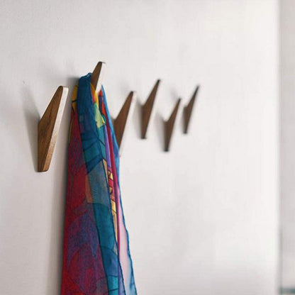 Row of darker wooden hooks on a white wall, with a colourful patterned scarf in red, blue and yellow hanging from one. 3