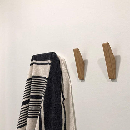 Two wooden hooks on a white wall beside a black and cream striped towel hanging from another hook. 4