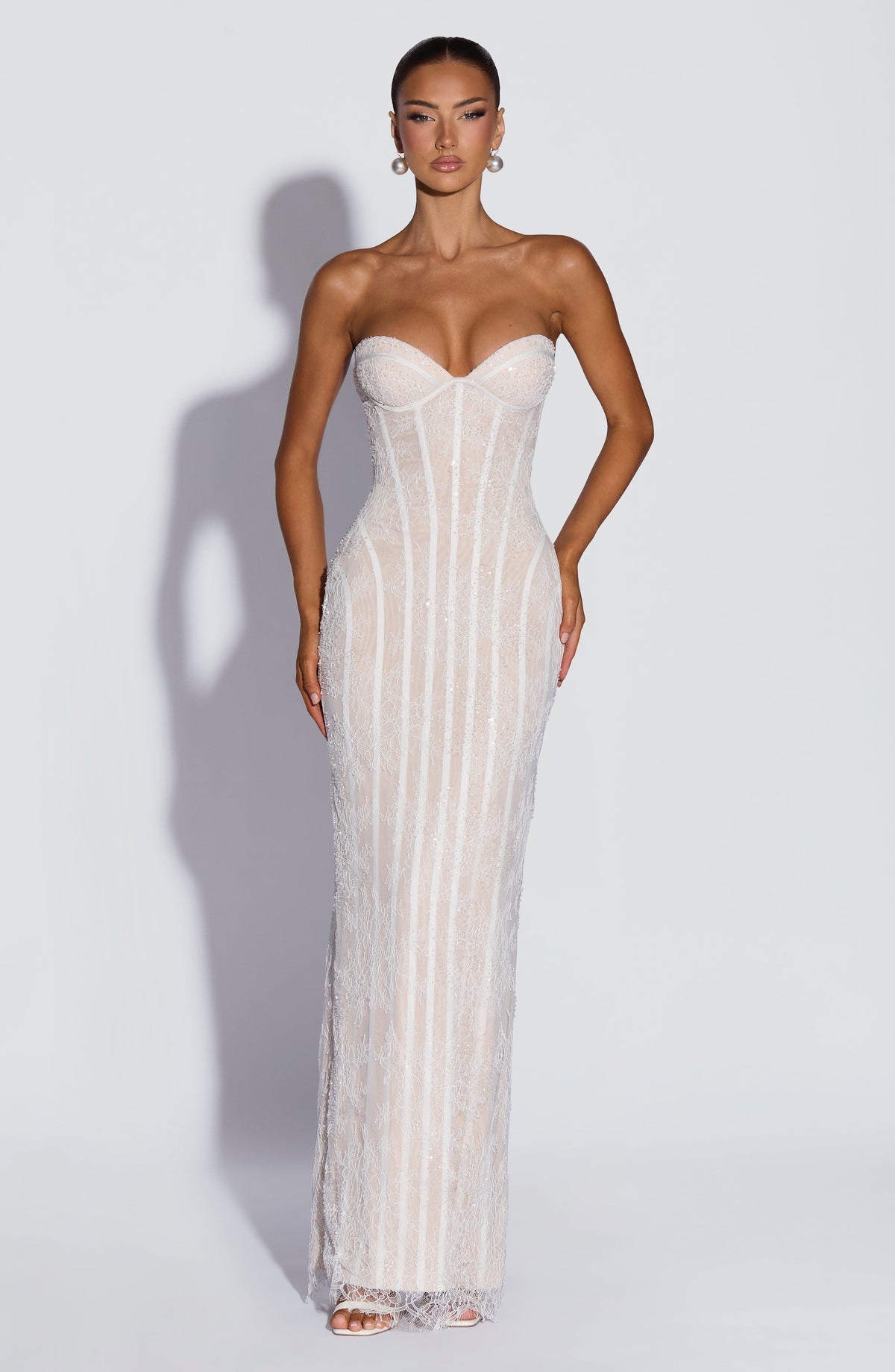 Front view of the white lace version over a nude lining, with beaded detailing and a sweetheart neckline, worn with pearl earrings. 9