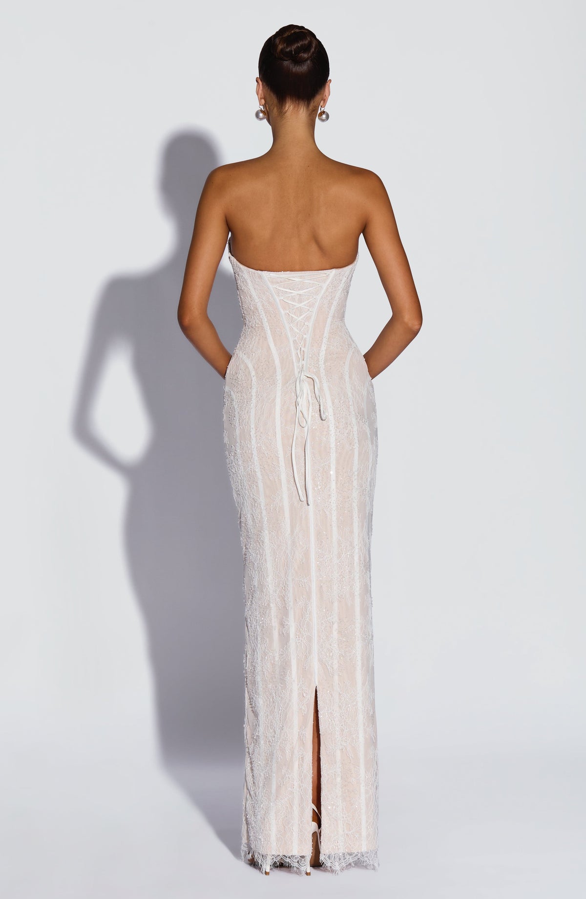 Back view of the white lace dress with corset lacing, trailing ribbon ties and a slit at the hem. 10