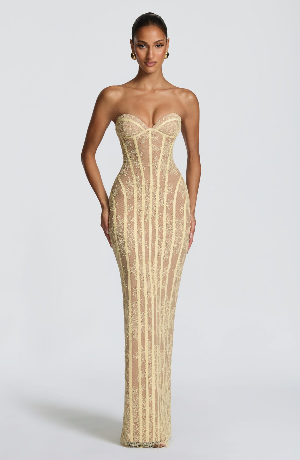 Front view of the pale yellow lace corset dress over a nude lining, with gold earrings and a slicked-back bun. 17