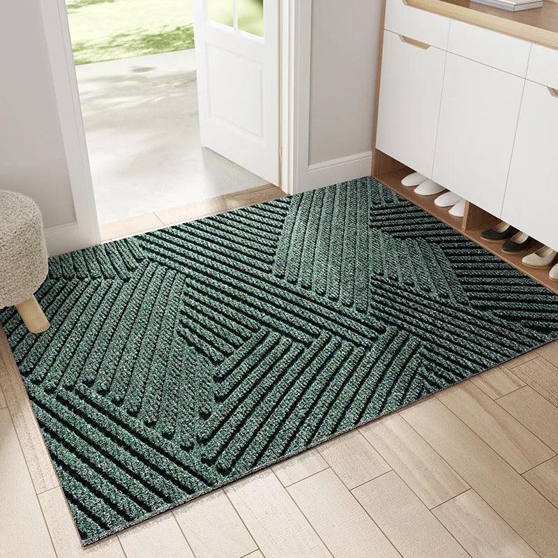 Green ribbed doormat with an angular geometric pattern, laid on light wood flooring inside an open front door beside a shoe cabinet. 1