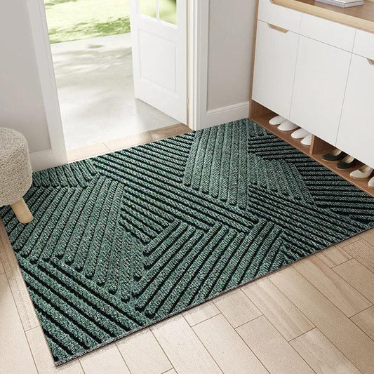 Green ribbed doormat with an angular geometric pattern, laid on light wood flooring inside an open front door beside a shoe cabinet. 1