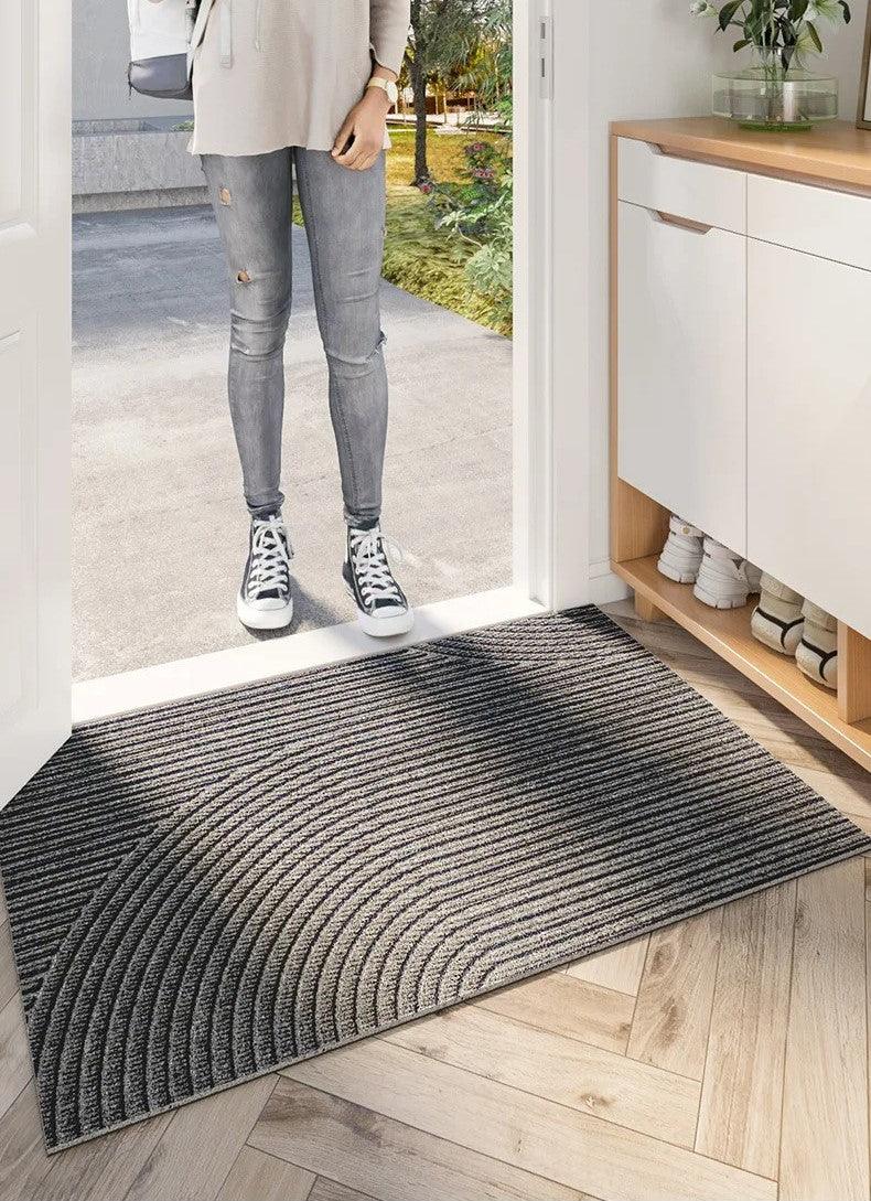 Dark grey and beige striped curved-pattern doormat at a front door threshold, with a person in jeans and trainers standing outside. 5