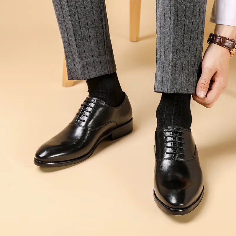 Black polished leather lace-up shoes worn with grey pinstripe trousers as the wearer adjusts his trouser leg 1