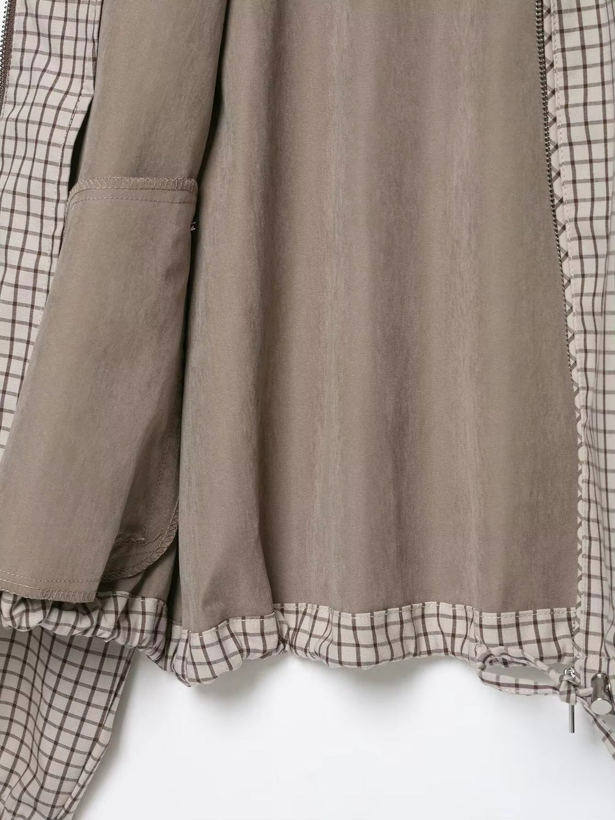 Inside of the jacket laid flat, showing the plain taupe lining, inner pocket and checked drawstring hem. 5