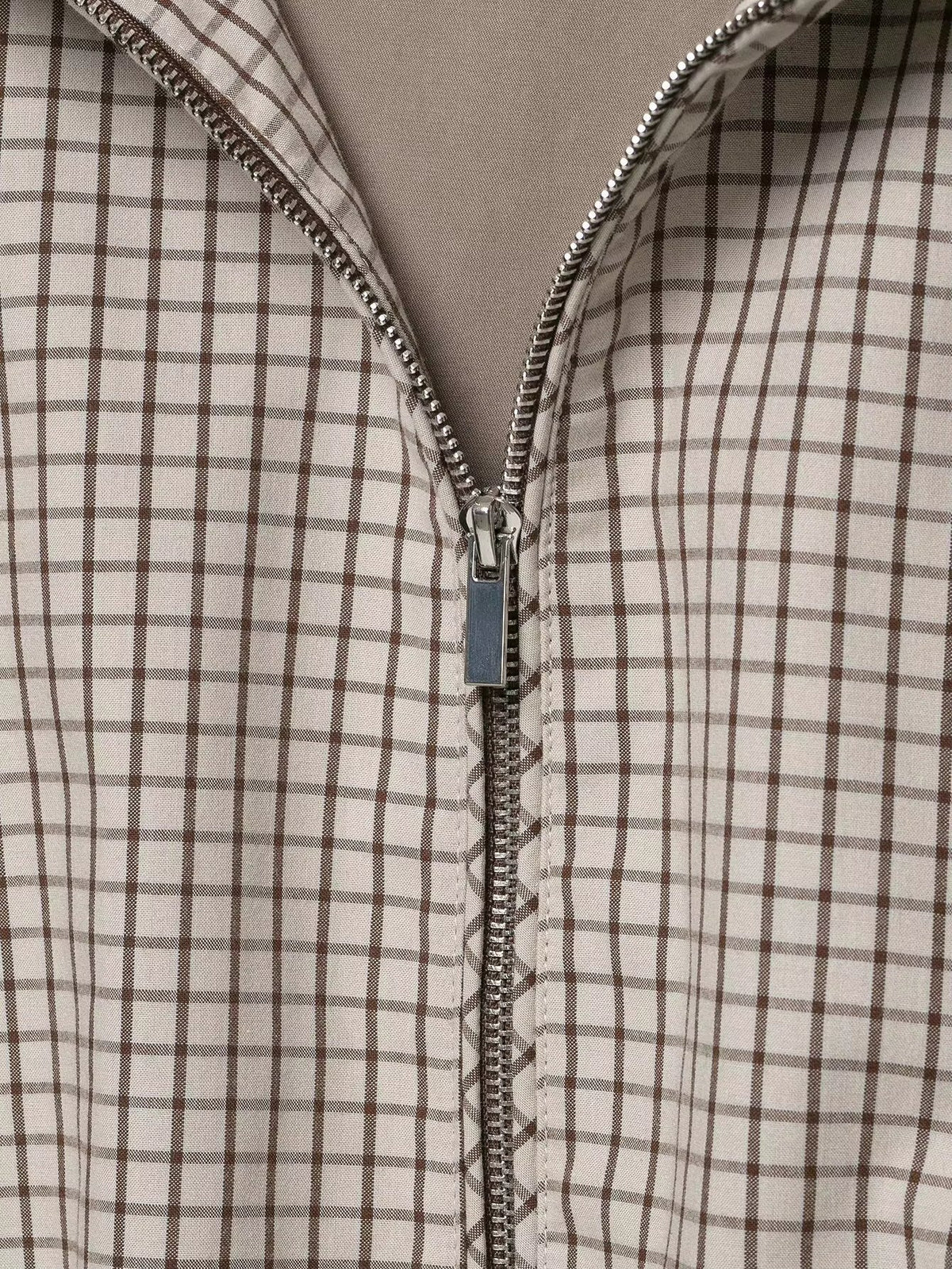 Close-up of the silver zip pull and metal teeth on the brown and cream checked fabric. 6