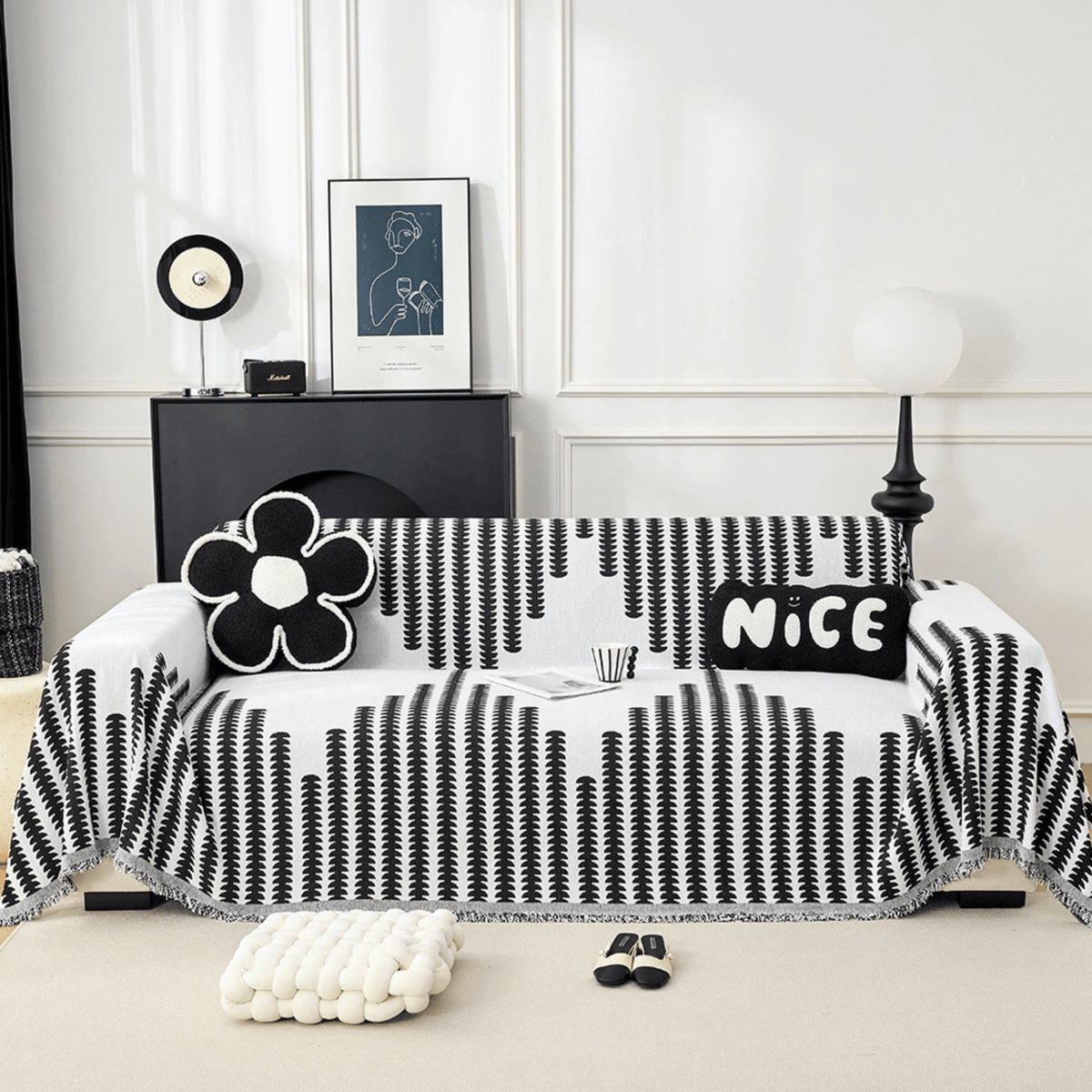 Black and white vertical-patterned chenille cover draped over a sofa, shown straight on with a flower cushion, a lettered cushion and fringed edges. 1
