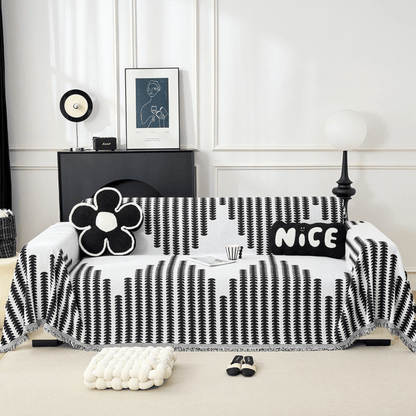 Black and white vertical-patterned chenille cover draped over a sofa, shown straight on with a flower cushion, a lettered cushion and fringed edges. 1