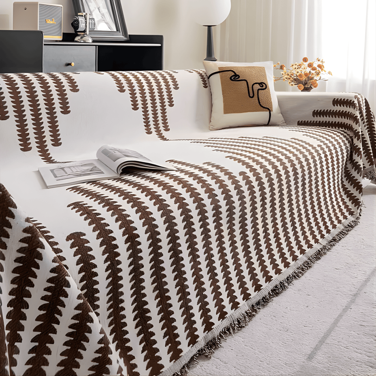Brown and cream colourway on a sofa, with a cushion showing an abstract line-art design and an open magazine on the seat. 9
