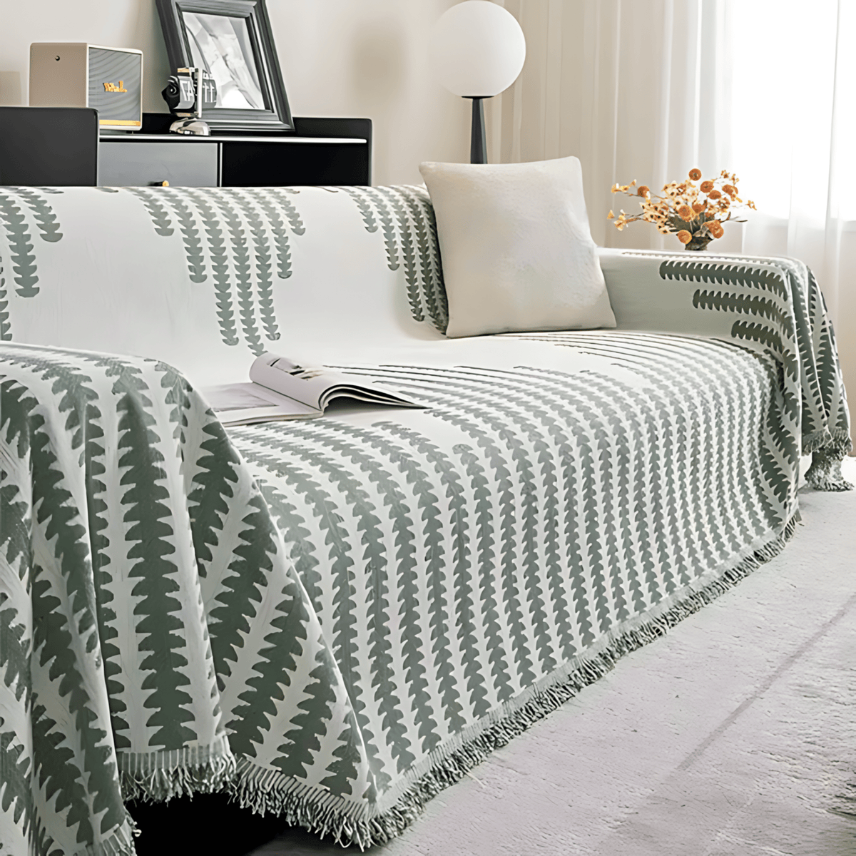 Sage green and cream colourway draped over a sofa, with fringed edges, a plain cushion and an open magazine. 10