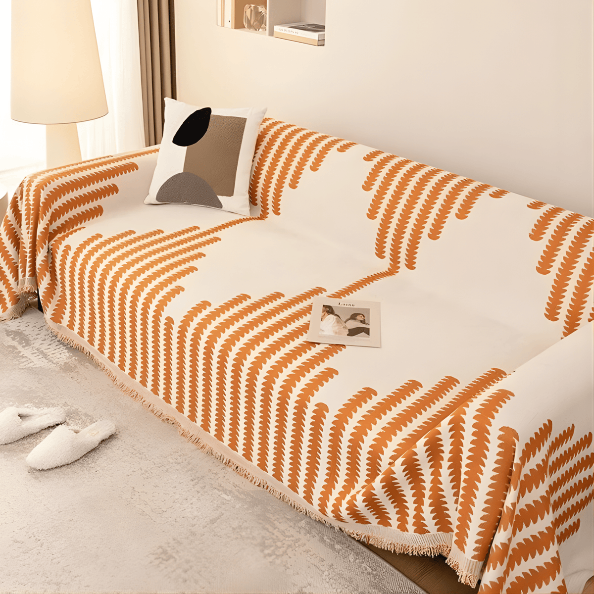 Orange and cream version of the cover seen from above on a sofa, with a geometric cushion and a magazine on the seat. 4