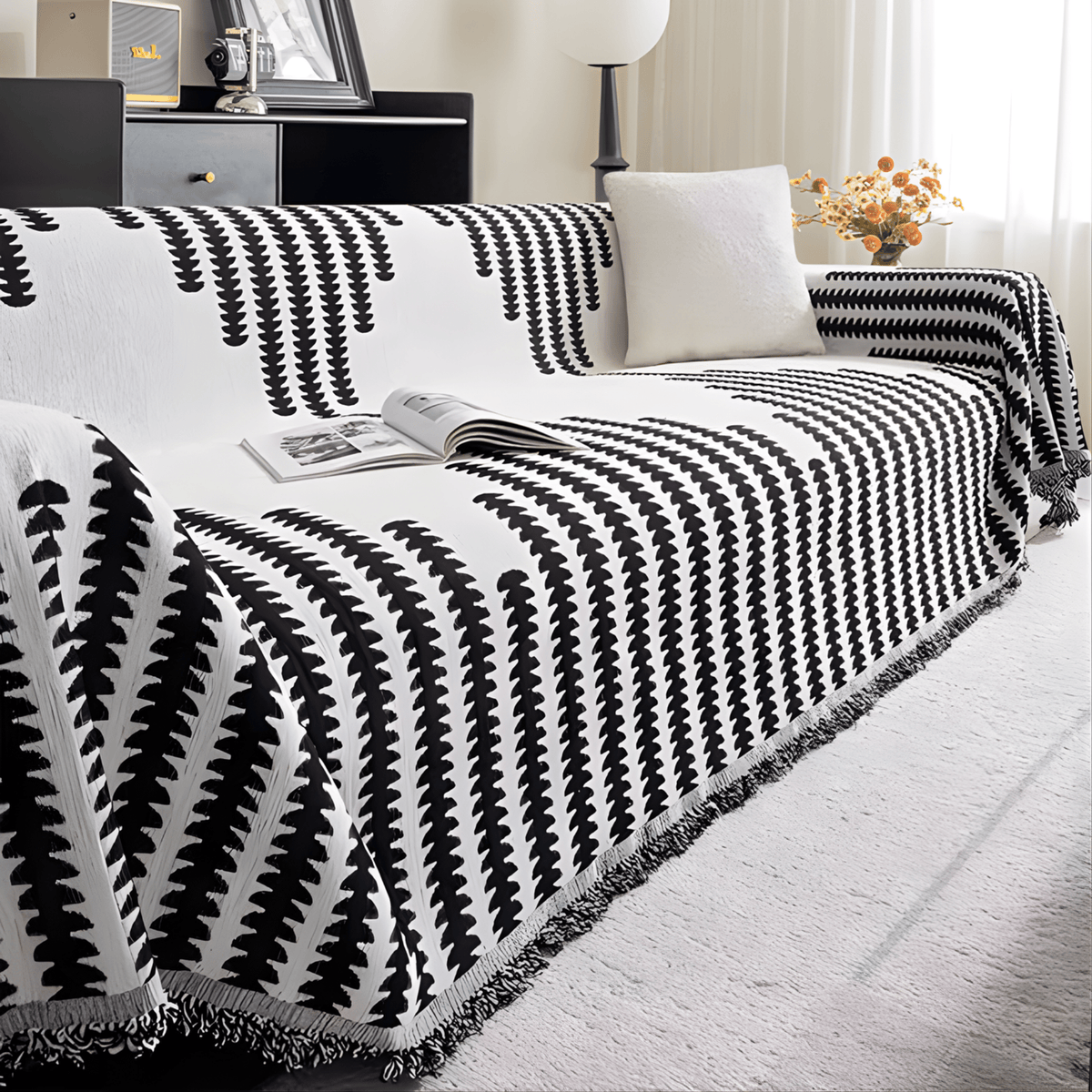 Black and white cover on a sofa from a low side angle, with a plain cushion, an open magazine and a vase of flowers. 6