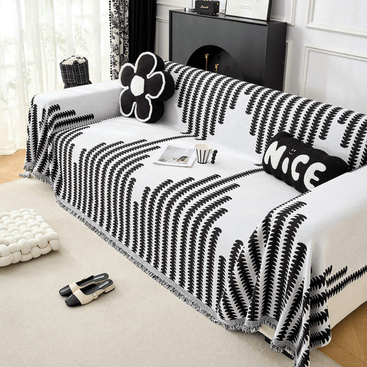 Black and white cover seen at an angle, covering the whole sofa including the arms, with a flower cushion and fringed hem. 5